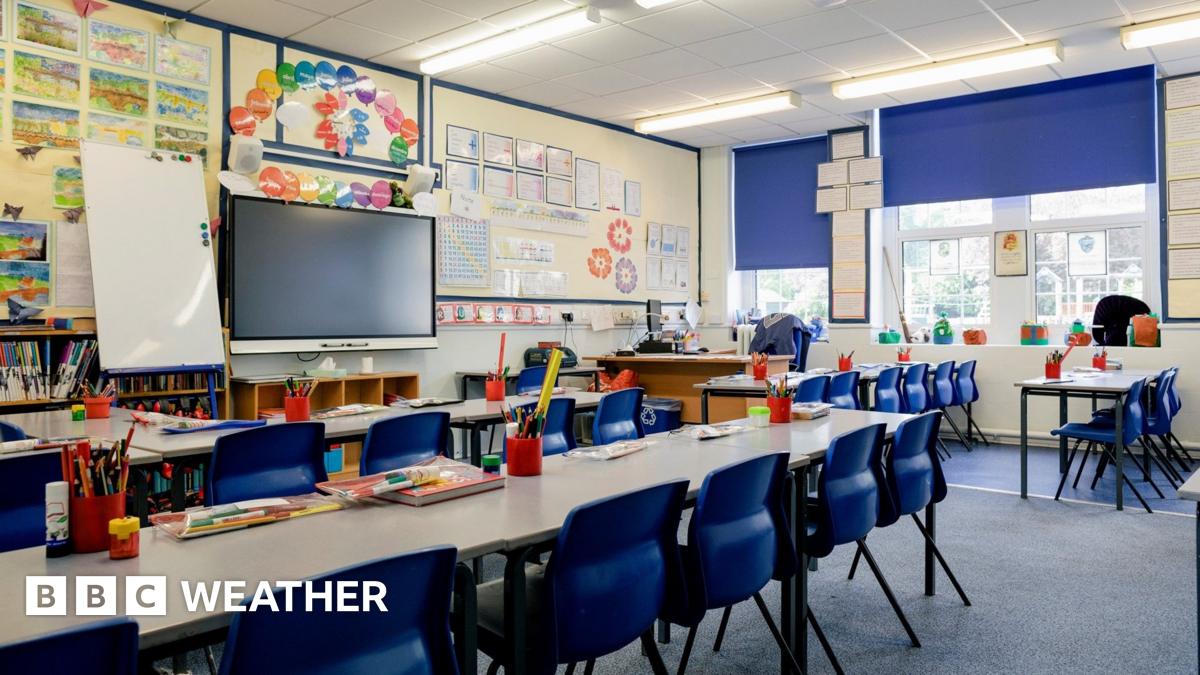 A bright, empty classroom with desks, chairs and pencils in the foreground